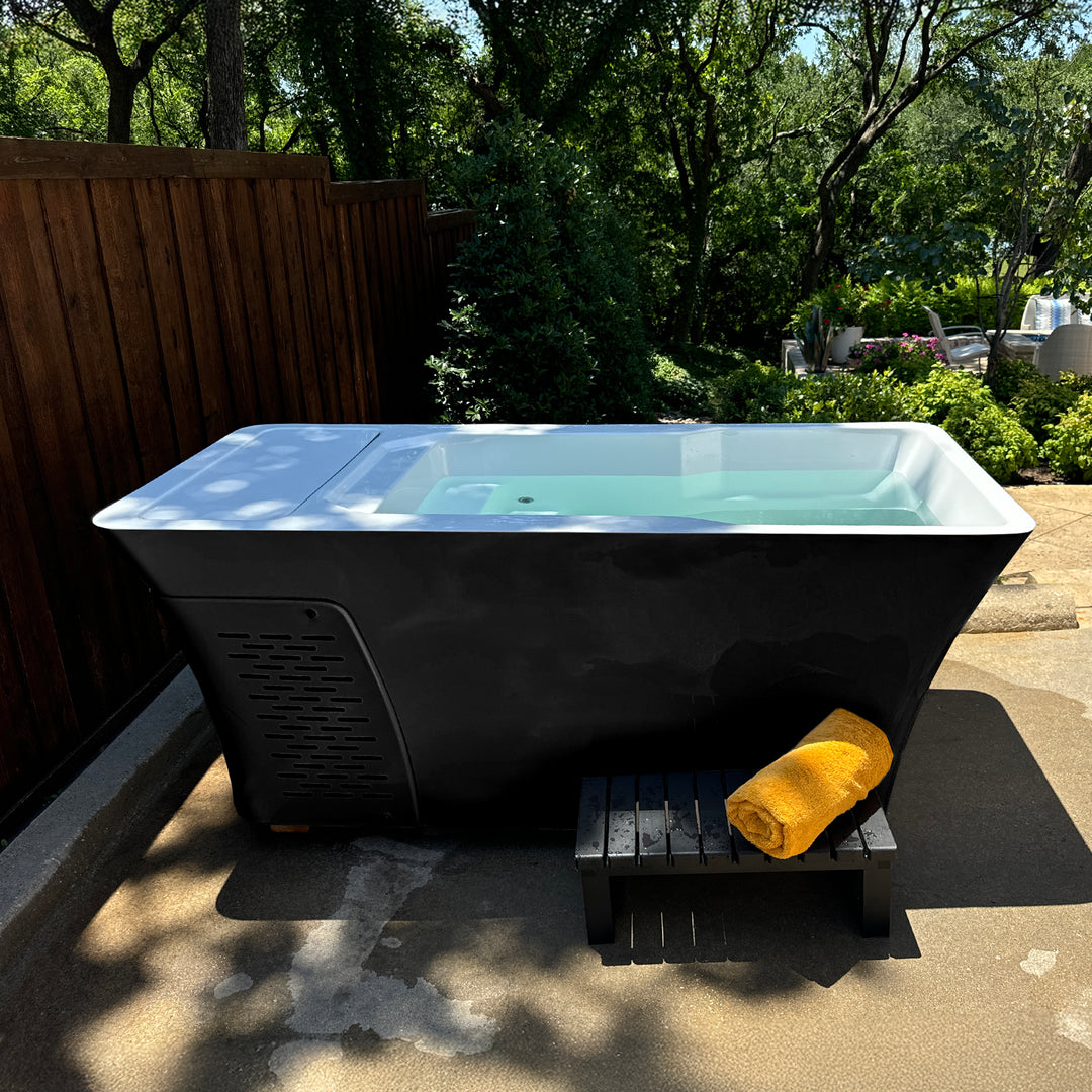 Snowbird Cold Plunge with stool and towel pictured in the outdoor backyard, with trees and fence in the background. 