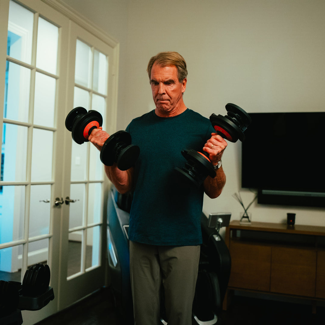 Man working out with one dumbbell in each hand doing dumbbell curls in his home. 