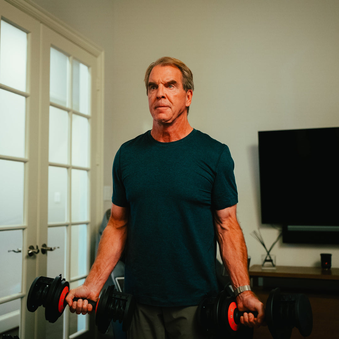 Man working out with one dumbbell in each hand doing dumbbell curls in his home. 